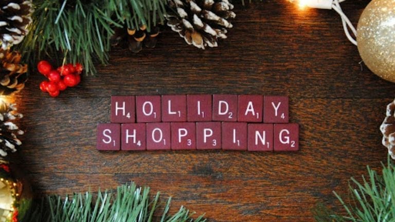 Scrabble tiles spelling “holiday shopping” in a Christmas wreath on a wooden table.